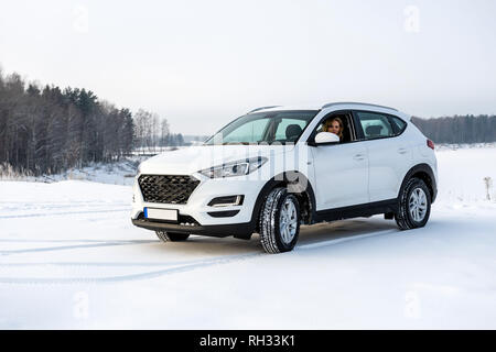 Die blonde Frau sitzt in einem weißen suv Auto in einem schneebedeckten Feld. Stockfoto