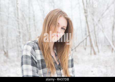 Junge Frau in Schwarz und Weiß Plaid Shirt stading in einem verschneiten Wald. Stockfoto