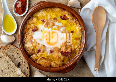 Knoblauch und Brotsuppe (Kastilisch, aus Spanien) in Lehmtöpfen und seine wichtigsten Bestandteile. Blick von oben. Holz Hintergrund Stockfoto