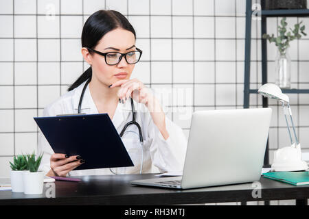 Weibliche brunette Arzt trägt eine Brille mit Tablet, intelligente und schöne Frau mit der Gadget und Stethoskop im weißen Büro Hintergrund. Stockfoto