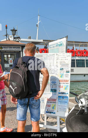 LAZISE, Gardasee, Italien - September 2018: Person Studium einen Aushang mit Informationen über fährzeiten und Reiseziele am Seeufer in Lazise Stockfoto