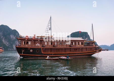 Zwei vietnamesische Frauen auf Ruderboote neben einem hölzernen Dschunke Boot mit Snacks und Getränken zu Touristen, Halong Bay, Vietnam Stockfoto