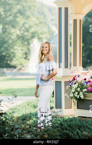 Eine attraktive blonde Haare kaukasischen High School senior posieren für ältere Bilder. Weibliche Teenager Portrait stand draußen im Park im Sommer. Stockfoto