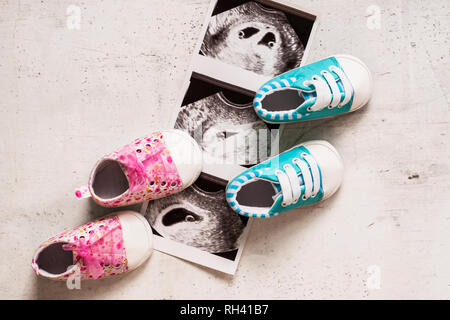 Blau und pink Booties neben Baby Fotos mit Ultraschall in der 4. Woche der Schwangerschaft. Warten auf Zwillinge. Sohn und Tochter. Selektiver Fokus Stockfoto