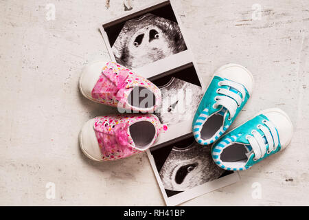 Blau und pink Booties neben Baby Fotos mit Ultraschall in der 4. Woche der Schwangerschaft. Warten auf Zwillinge. Sohn und Tochter. Selektiver Fokus Stockfoto