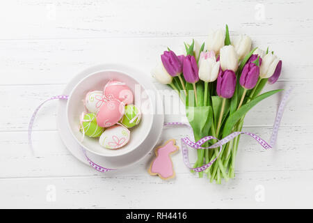 Ostern Grußkarte mit Tulpe Blumen Blumenstrauß, Ostereier und Hasen Cookie. Draufsicht über weiße Holztisch Stockfoto
