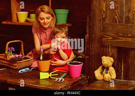 Spritzen Konzept. Mutter und Sohn Sprühwasser auf Topfpflanze. Mutter und Kind spritzen Frühling Blumen im Topf. Spritzen Wasserflasche oder Spritze. Stockfoto