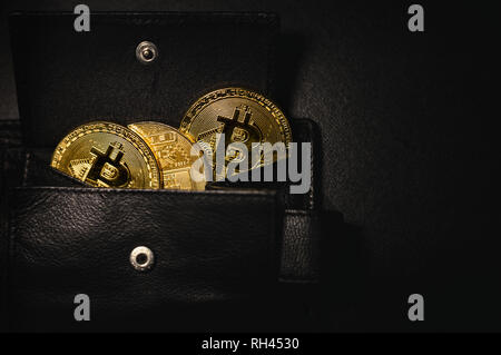 Portemonnaie voller shinning Münzen der cryptocurrency (golden Bitcoins) auf schwarzen und dunklen Hintergrund. Stapel von crypto Münzen in der Mappe gespeichert. Stockfoto
