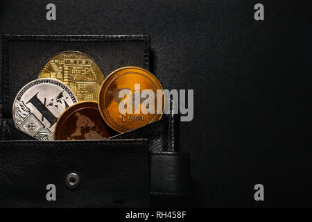 Portemonnaie voller shinning Münzen der cryptocurrency (golden Bitcoin, litecoin, Welligkeit) auf schwarzen und dunklen Hintergrund. Stapel von crypto Münzen in der Mappe gespeichert. Stockfoto