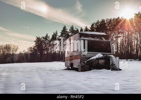 Schönes Foto von Alten und Verlassenen Wohnwagen mitten in der verschneiten Wiese im Winter. Beleuchtete Caravan (Wohnmobil) - außerhalb der Saison Stockfoto