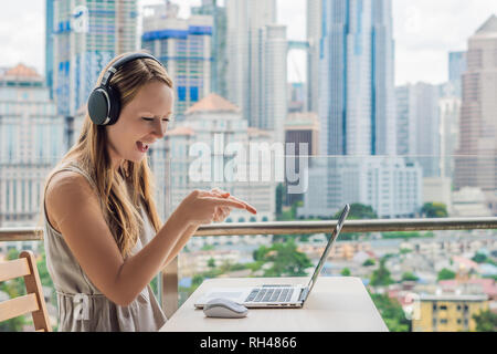 Junge Frau lehrt eine Fremdsprache lernt eine Fremdsprache im Internet auf ihrem Balkon vor dem Hintergrund einer großen Stadt. Online Sprache Stockfoto