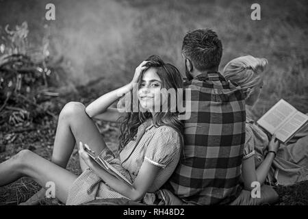 Camping in der Wildnis. Drehen Sie wieder Kerl auf der Suche nach Feuer, während zwei hübsche Mädchen Buch lesen. Smiling brunette mit klammern sich an ihre Freundin. Stockfoto