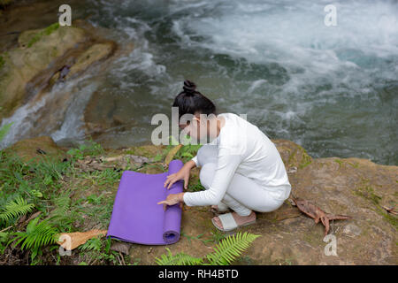 Frauen tragen ein weißes Kleid rollen Yoga Yoga am Wasserfall. Stockfoto