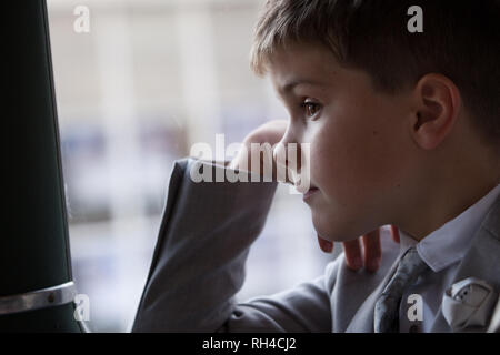 Junge Suite tragen, mit kurzen braunen Haaren auf der Suche aus dem Fenster des fahrenden Fahrzeugs. Stockfoto