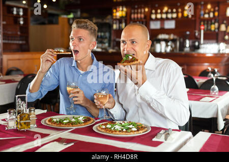 Zwei glückliche Männer emotional Sport im TV beim essen Pizza mit Weißwein im gemütlichen Restaurant Stockfoto