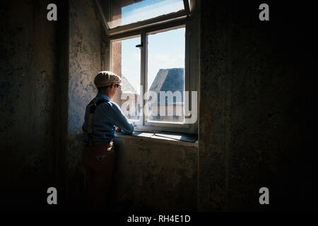 Junge, der aus dem sonnigen Fenster schaute Stockfoto