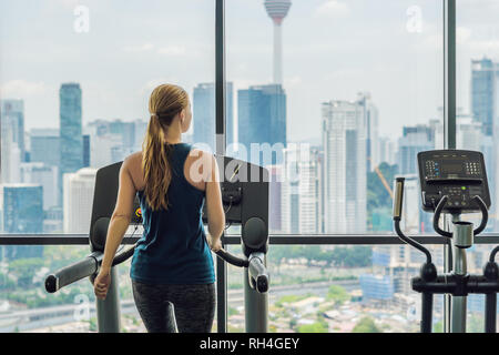 Sport, Fitness, Lifestyle, Technik und Mensch Konzept - Frau Ausübung auf Laufband im Fitnessstudio vor dem Hintergrund einer großen Stadt Stockfoto