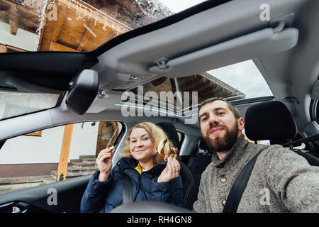 Junges Paar unter selfie in einem Auto mit Glasdach. Weitwinkelobjektiv gedreht. Bärtiger Mann und blonde Frau lächelnd. Stockfoto