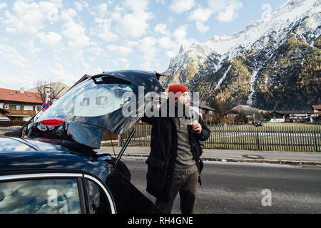 Mann seinen Rucksack aus schwarzem Kofferraum mit Blick auf die Berge im Bayerischen Mittenwald, Deutschland Die Bärtigen Stockfoto