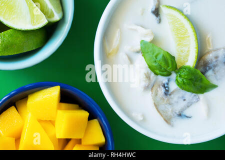 Ansicht von oben von Thai Food - Tom Kha Gai Suppe, Mango, und Limetten in runde Schalen auf grüne Fläche. Stockfoto