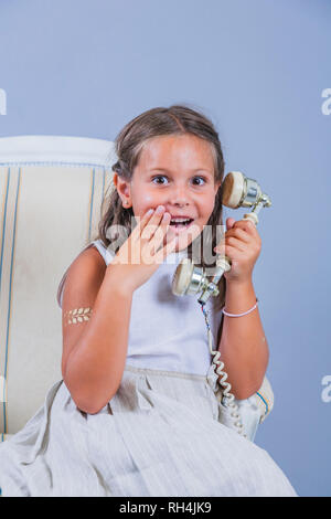 Mädchen im Kleid im Gespräch mit alten Telefon mit überraschten Gesicht Stockfoto