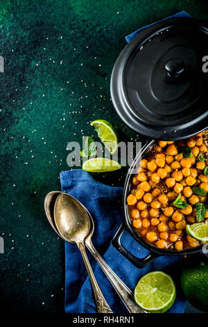 Vegan indisches Essen, süsse Kartoffeln und Kichererbsen in Curry, Chana Masala mit Kalk Schichten und Gewürzen auf dunkelgrünen Tischplatte ciew Platz kopieren Stockfoto