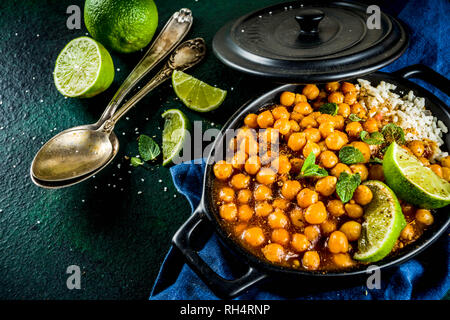 Vegan indisches Essen, süsse Kartoffeln und Kichererbsen in Curry, Chana Masala mit Kalk Schichten und Gewürzen auf dunkelgrünen Tischplatte ciew Platz kopieren Stockfoto