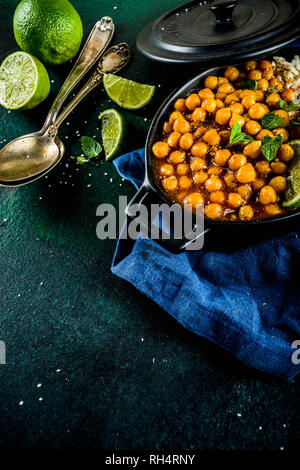 Vegan indisches Essen, süsse Kartoffeln und Kichererbsen in Curry, Chana Masala mit Kalk Schichten und Gewürzen auf dunkelgrünen Tischplatte ciew Platz kopieren Stockfoto