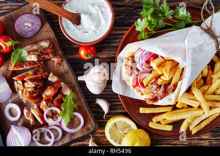 Griechische Souvlaki, Gyros Pita ma mit Hühnerfleisch, Gemüse, Pommes frites und Joghurt, Knoblauch Sauce Zutaten auf einem Schneidebrett auf einem rustikalen Tisch, v Stockfoto