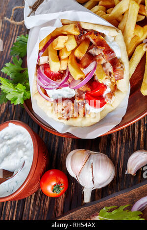 Close-up der griechischen Souvlaki, Gyros Pita ma mit Hühnerfleisch, Gemüse, Pommes frites und Joghurt, Knoblauch Sauce Zutaten auf einem Schneidebrett auf einem Rus Stockfoto