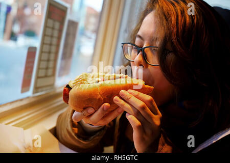 Junge Frau mit einem guten Spezialität Hot Dog mit einer fantastischen Mischung aus toppings perfekt für die kalte Winter Wind. Stockfoto