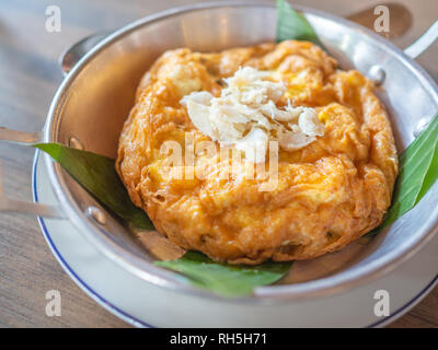 Leckere Thai Stil Omelett mit Krabben Fleisch an der Spitze. Close-up Krabbenfleisch Topping auf omelett Dekoration mit Banana Leaf in Aluminium Pfanne und weißem Porzellan Stockfoto