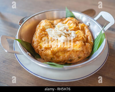 Leckere Thai Stil Omelett mit Krabben Fleisch an der Spitze. Krabbenfleisch Topping auf omelett Dekoration mit Banana Leaf in Aluminium Pfanne und weißem Porzellan Platte auf Stockfoto