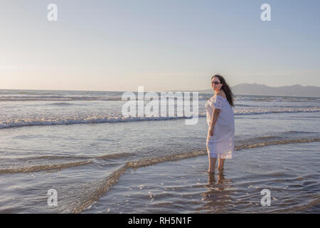 Mexikanische Frau in einem weißen Kleid und Sonnenbrille geniessen das Wasser im Meer an einem wunderschönen sonnigen Tag am Strand in Puerto Vallarta, Jalisco, Mexiko Stockfoto