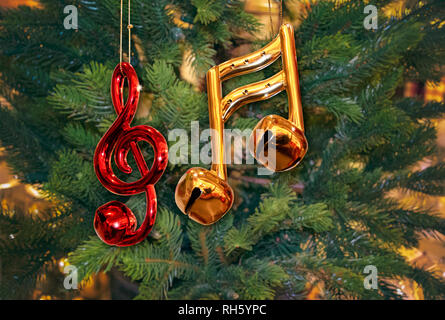 Glänzendes Rot Violinschlüssel Ornament und Gold Noten mit Glocken auf grüner Weihnachtsbaum Stockfoto