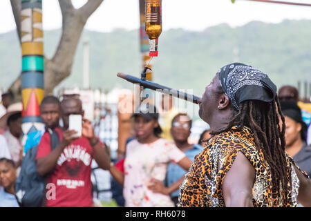 Durban, Südafrika - 6. Januar 2019: Ein schwarzer Mann, der Feuer-Swallower Ausgleichen einer Flasche am Strand von Durban, Südafrika. Stockfoto