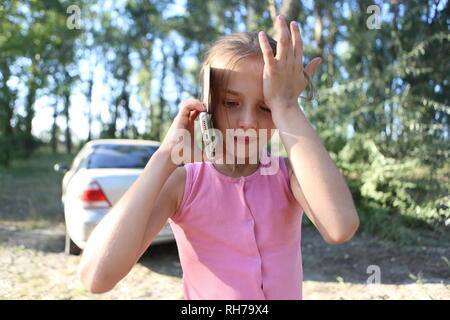 Auf dem Hintergrund der Natur ein kleines Mädchen emotional Unterhaltung am Telefon mit einem Freund Stockfoto