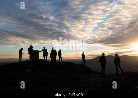 Menschen auf dem Gipfel des Arthur's Seat in Edinburgh, beobachten den Sonnenuntergang über der Stadt. Arthur's Seat ist ein Wahrzeichen Hügel in der Mitte des Holyrood Park, einem beliebten Aussichtspunkt mit Blick auf Edinburgh. Stockfoto