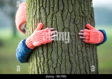 Frau mit Handschuhen umarmt Baum im Winter zu Fuß auf dem Land Stockfoto