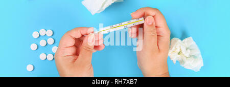 Ein Mann hält ein Thermometer in seine Hand mit einer hohen Temperatur vor einem blauen Tisch mit Tabletten. Top Anzeigen, Kopieren, flach Stockfoto