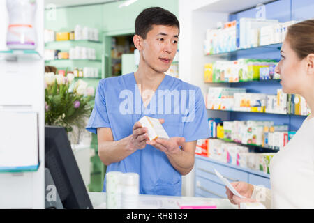 Froh, Frau, Kunde fragt koreanischen Mann Apotheker über Arzneimittel, die in der Nähe der Kasse in der Apotheke Stockfoto