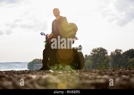 Biker Mensch und Motorrad mit Fluss Hintergrund, Reiter moto Reise auf der Straße am Flußufer, genießen Freiheit und aktiven Lebensstil. Stockfoto