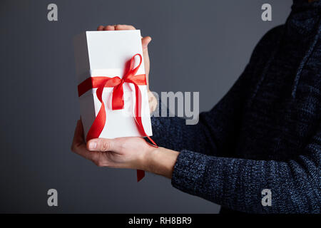 Weiß Geschenkbox mit roter Schleife in männlichen Händen. Soft Focus Stockfoto