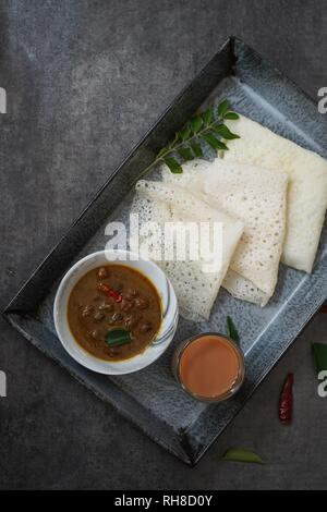 Neer Dosa/South Indian Reis Crepes mit Channa curry Tee auf einem Tablett serviert. Stockfoto