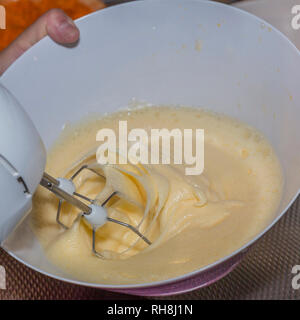 Elektrische Mixer schlagen einige Eier mit Zucker in eine Schüssel für einen Kuchen Stockfoto