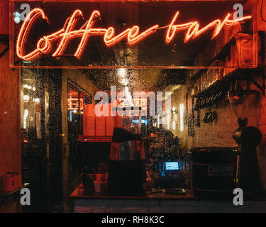 London, Großbritannien - 26 Januar, 2019: Beleuchtete Fenster und Leuchtreklame auf eine Coffee Bar in Canary Wharf an einem regnerischen Abend. Canary Wharf ist ein beschäftigter Finanzielle ein Stockfoto
