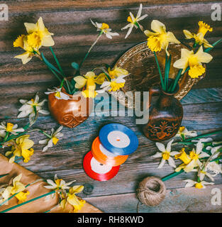 Narzissen Blumen in Keramik Krüge und auf einem Tisch verstreut, Kraftpapier und bunten Bändern auf einem hölzernen Tisch in einer retro rustikalen Stil Stockfoto