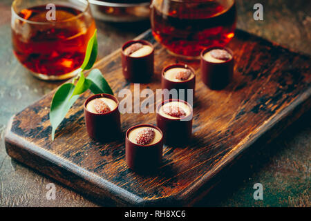 Glas transparent Teekanne und zwei Glas Tassen mit schwarzem Kaffee mit Schokolade Süßigkeiten Sortiment onwooden cutboard Stockfoto