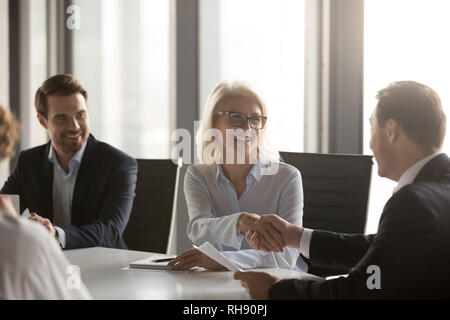 Gerne reife Geschäftsfrau handshaking neuen männlichen Partner bei Konferenz Stockfoto