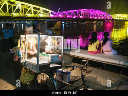 Hue, Vietnam; Straßenverkäufer mit Trang Tien Brücke bei Nacht beleuchtet Stockfoto